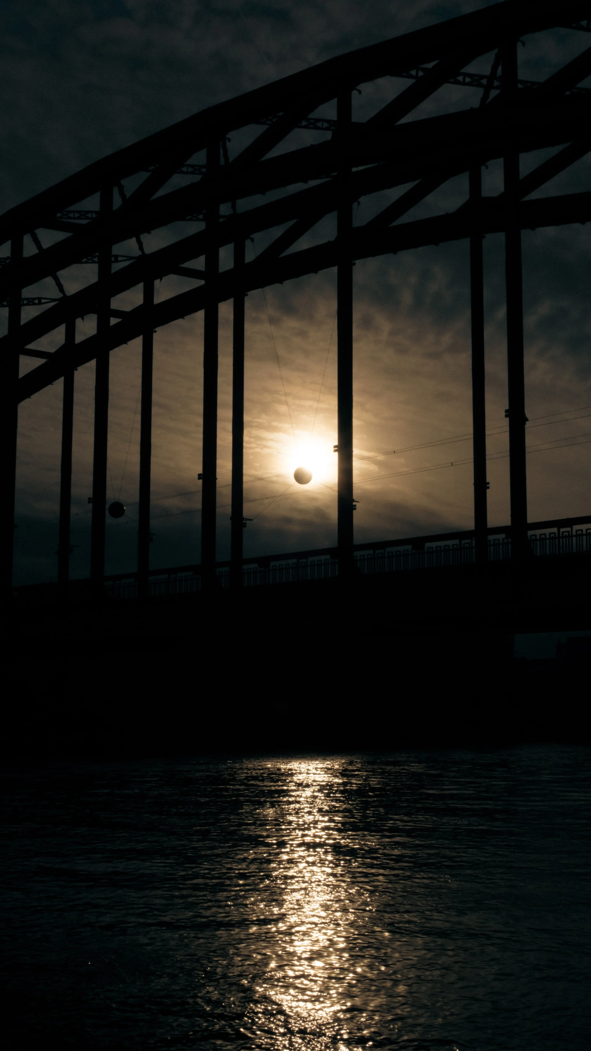 Schatten einer Eisenbahnbrücke bei Sonnenuntergang, die Sonne steht hinter der Brücke, Reflexion im Wasser.
