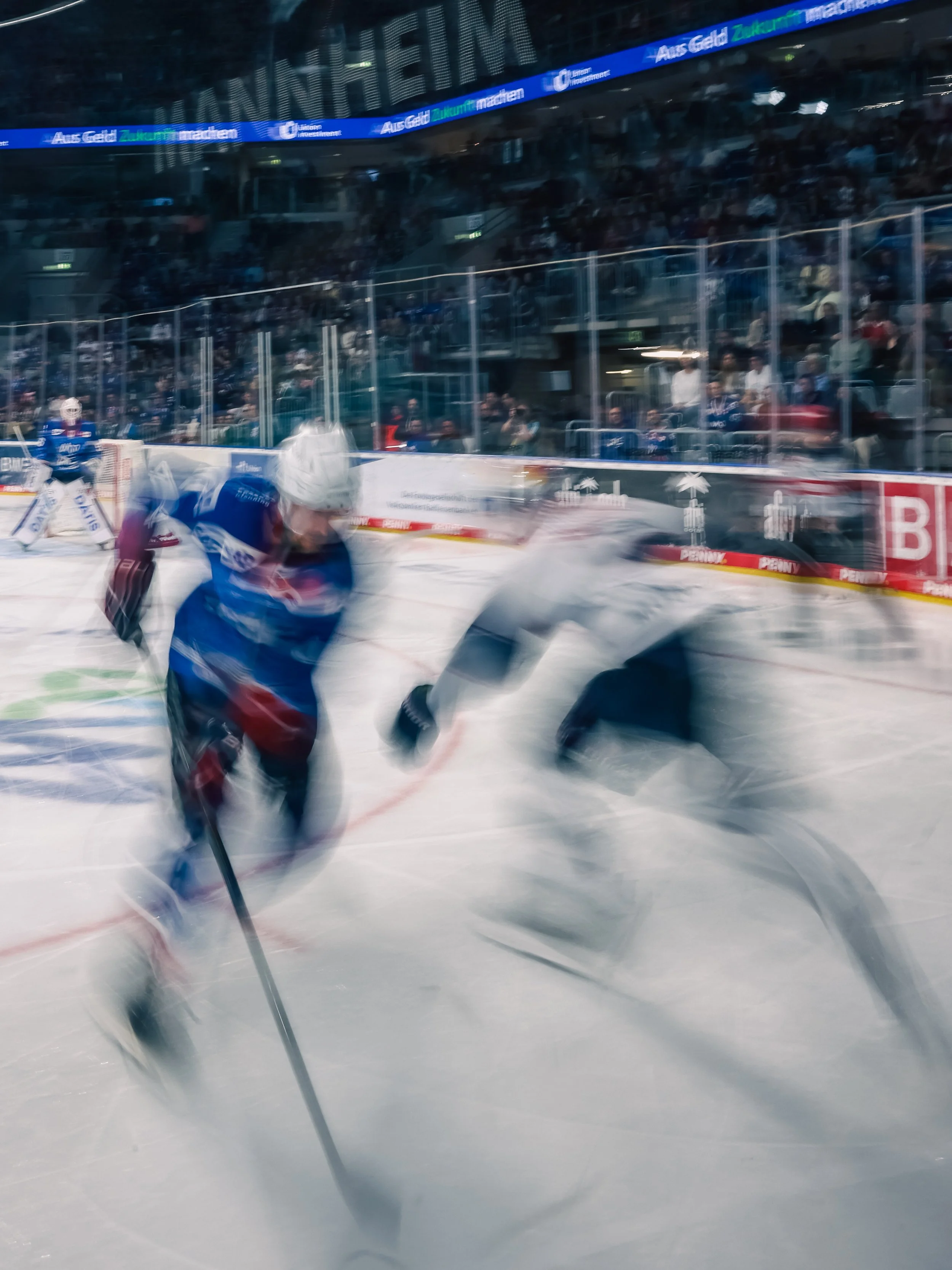 Eishockeyspieler in Bewegung auf dem Eis, im Hintergrund das Publikum im Stadion. Künstlerisch durch Langezeitbelichtung bzw. Slow Shutter.