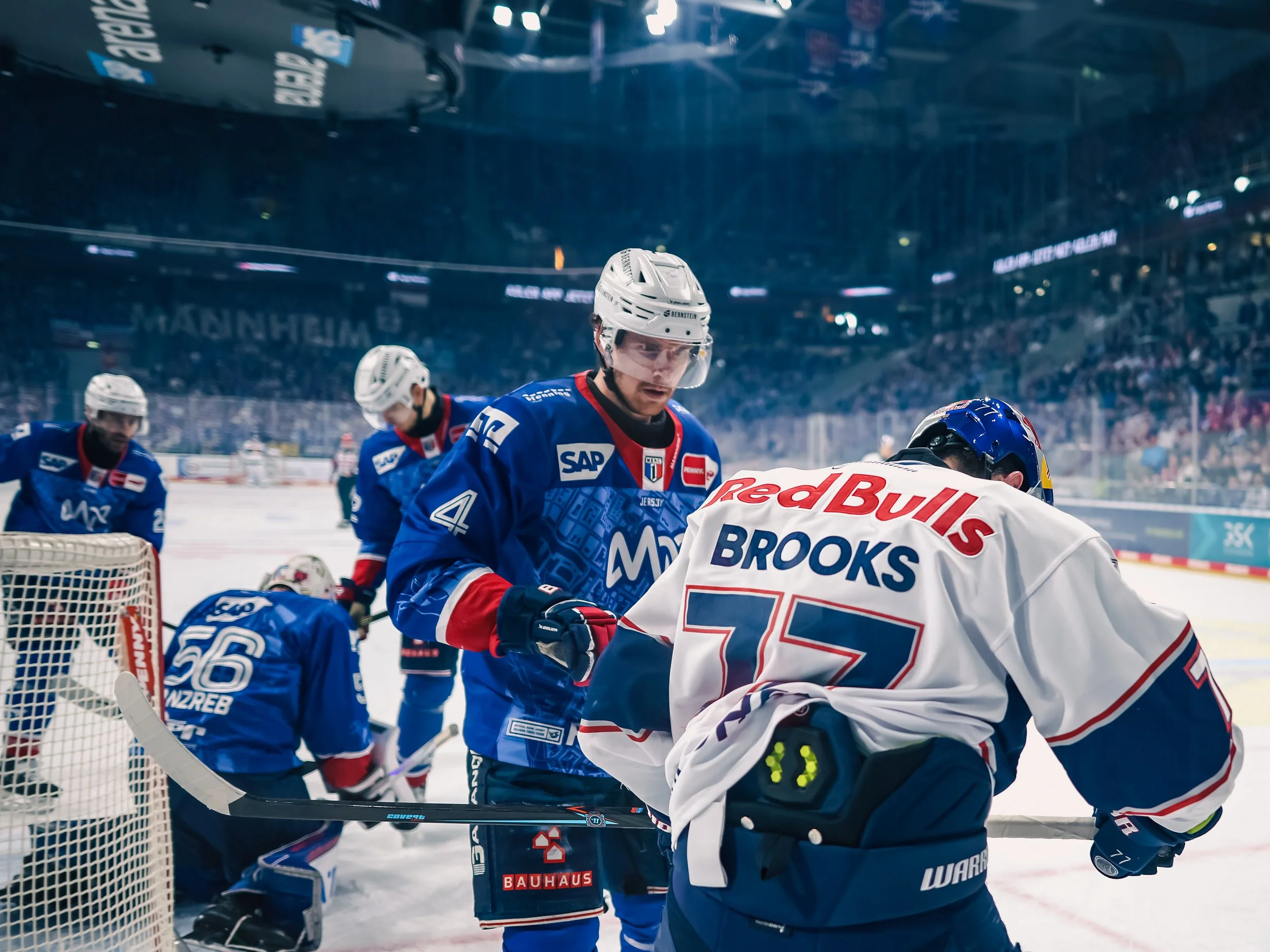 Eishockeyspieler von Adler Mannheim und Red Bull München auf dem Spielfeld zeugen Emotionen, nahe dem Tor, während eines Spiels. Sportfotografie bei den Adler Mannheim.