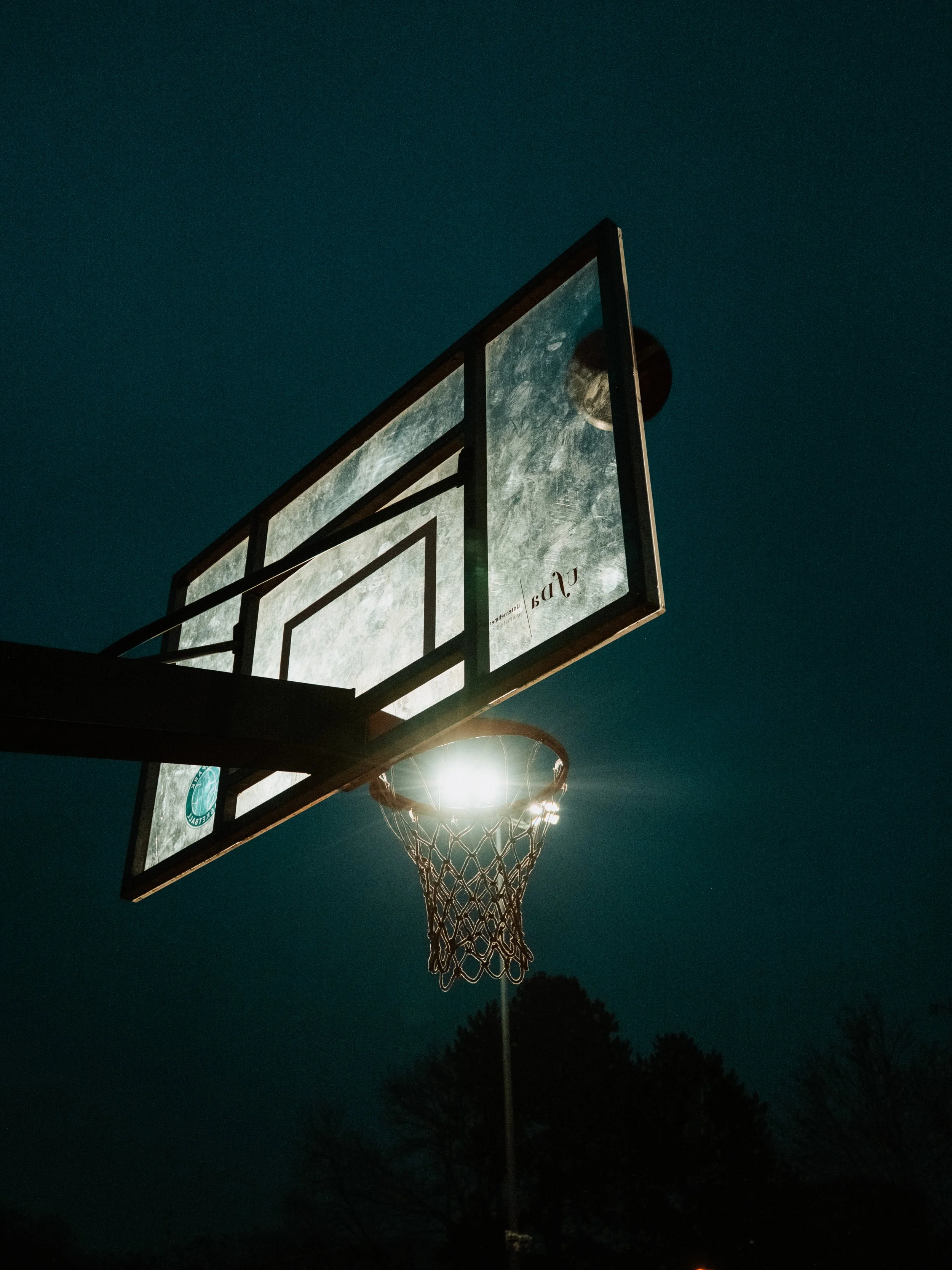 Ein Basketballkorb bei Nacht, beleuchtet vom Mond, mit dunklem Himmel im Hintergrund.