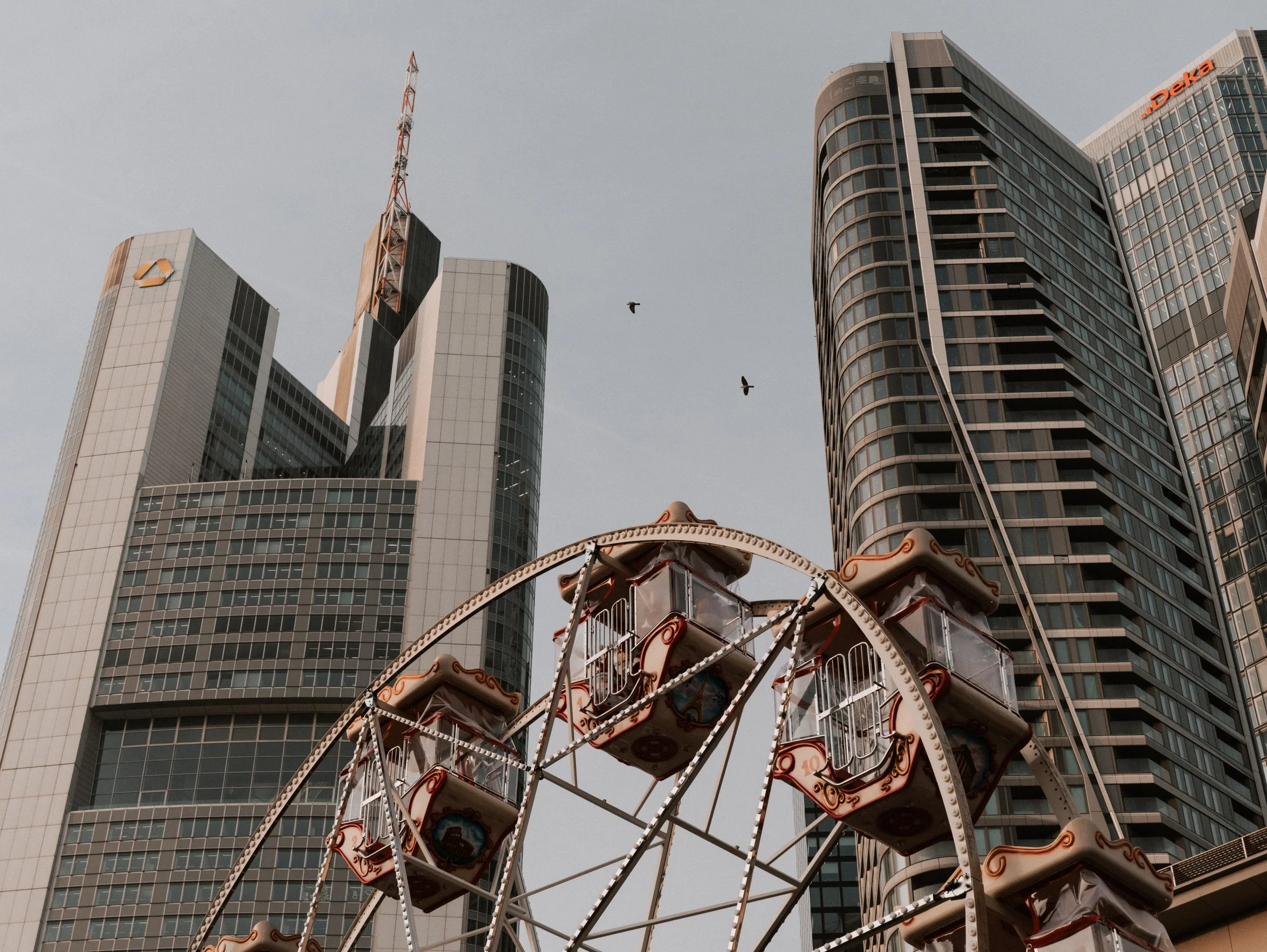 Hochhäuser von Frankfurt und ein Karussell im Stadtzentrum, zwei Vögel fliegen am Himmel.
