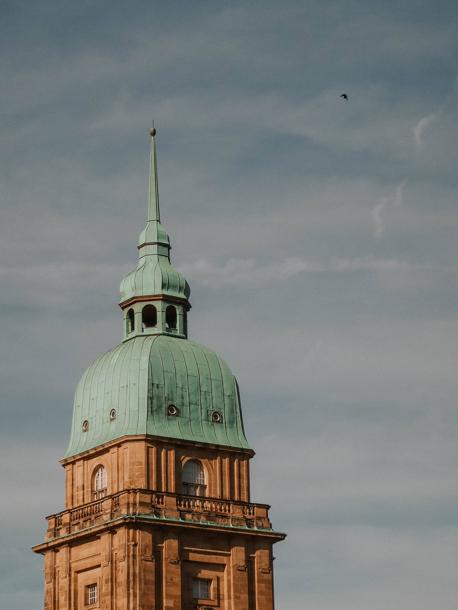 Hessisches Landesmuseum in Darmstadt, Hessen, mit grünem Kupferdach gegen einen bewölkten Himmel, mit einem Vogel in der Luft.