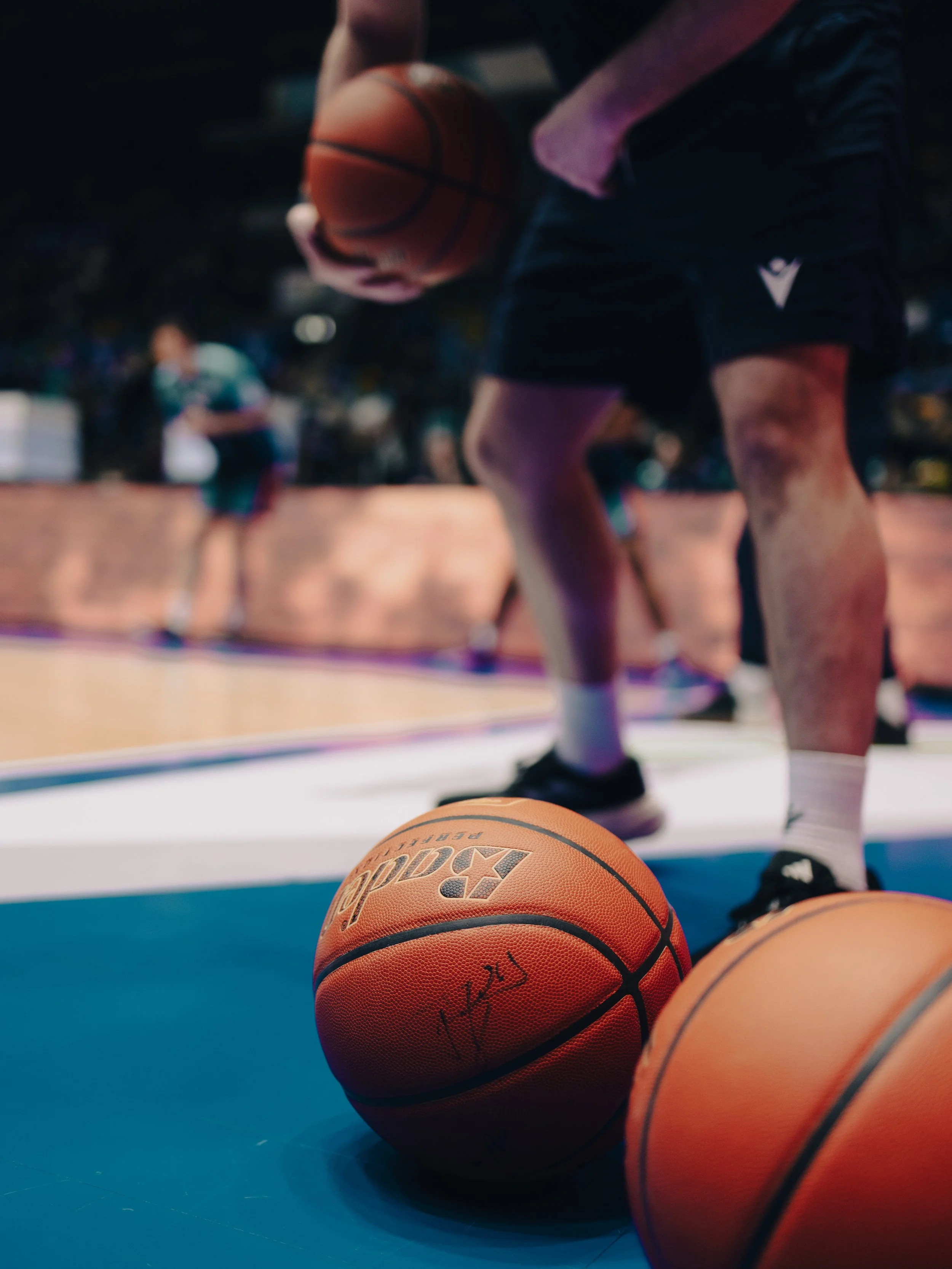 Blick auf mehrere Basketballs auf dem Boden eines Basketballfeldes, mit einem Spieler im Hintergrund.