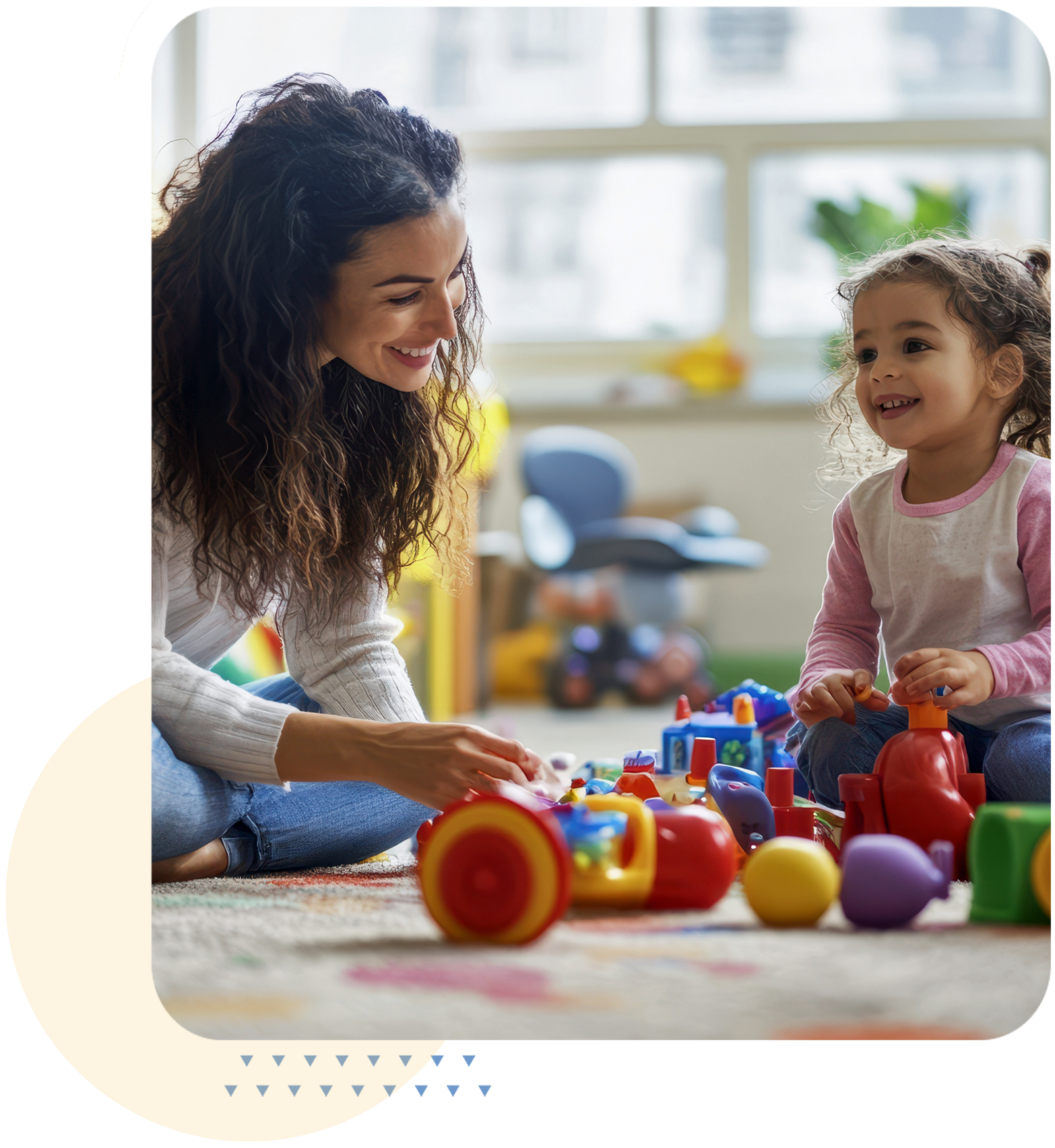 A young woman and a little girl playing with colorful building toys on a carpet in a bright room with large windows and houseplants.