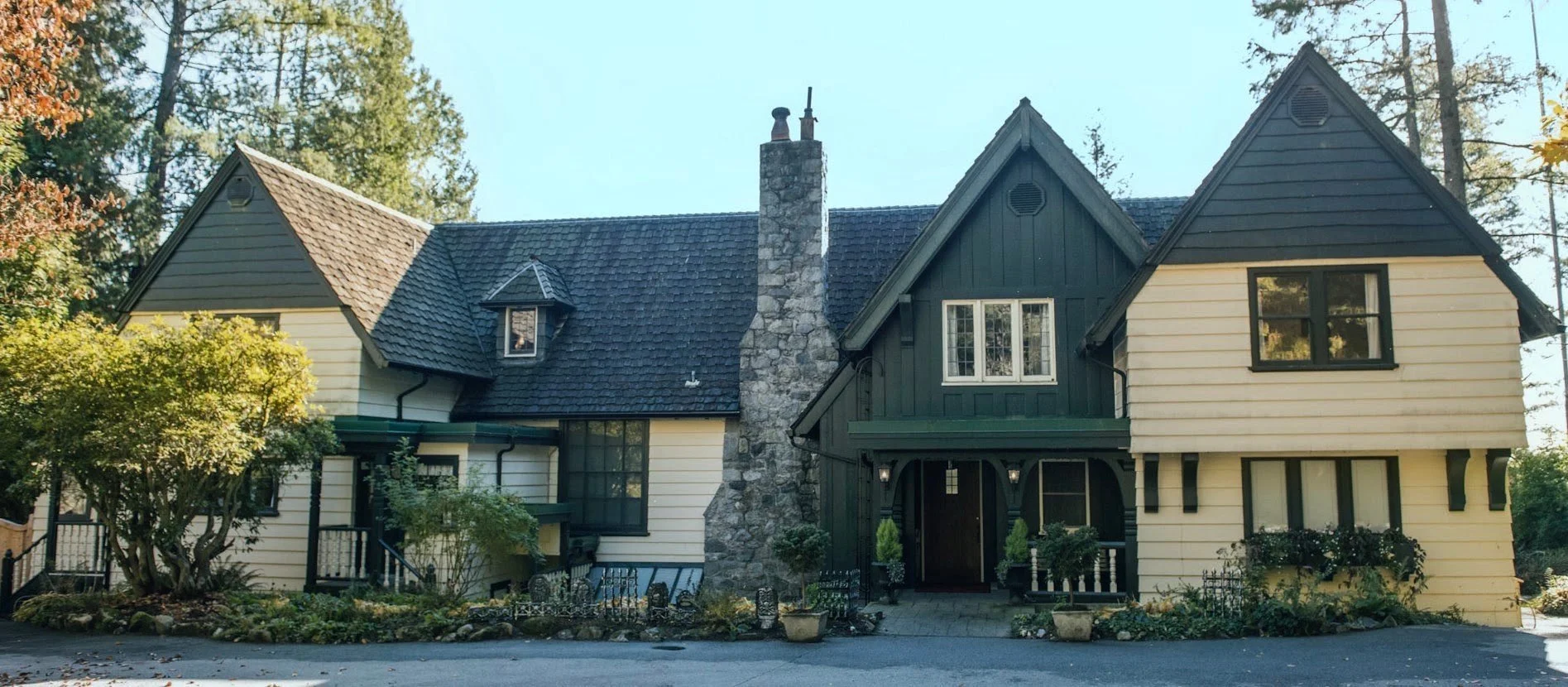 The full front façade of Minnekhada Lodge, with cream siding, green gables and a stone chimney