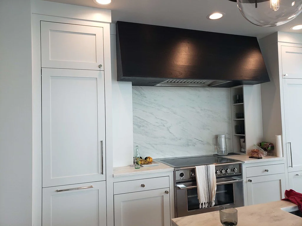 Modern white kitchen with built-in cabinets, a marble backsplash, a stainless steel oven, and a black range hood.