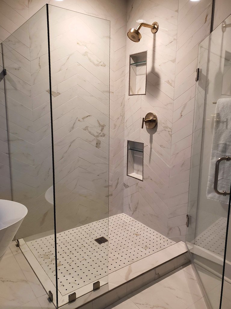 Modern glass-enclosed shower with marble tiles, brass fixtures, and built-in niches for toiletries.