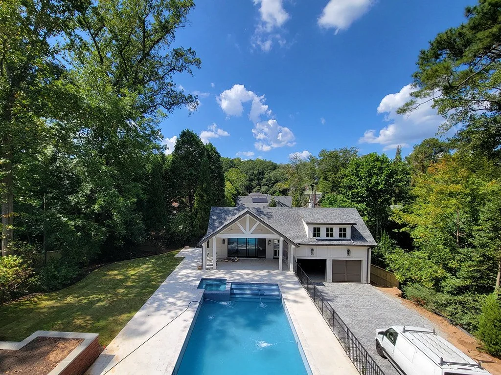 Modern house with a backyard swimming pool, surrounded by trees, with a driveway and a white van parked nearby.
