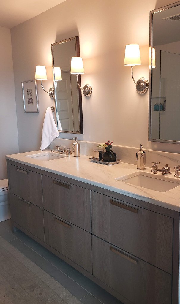 Modern bathroom vanity with two sinks, marble countertop, two large mirrors, wall-mounted lights, and decorative accents.