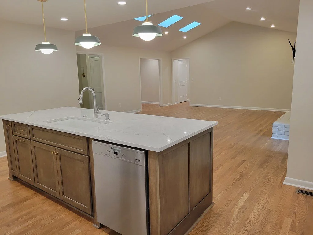 Open-concept living space with a kitchen island, hardwood floors, high vaulted ceiling with skylights, and recessed lighting.