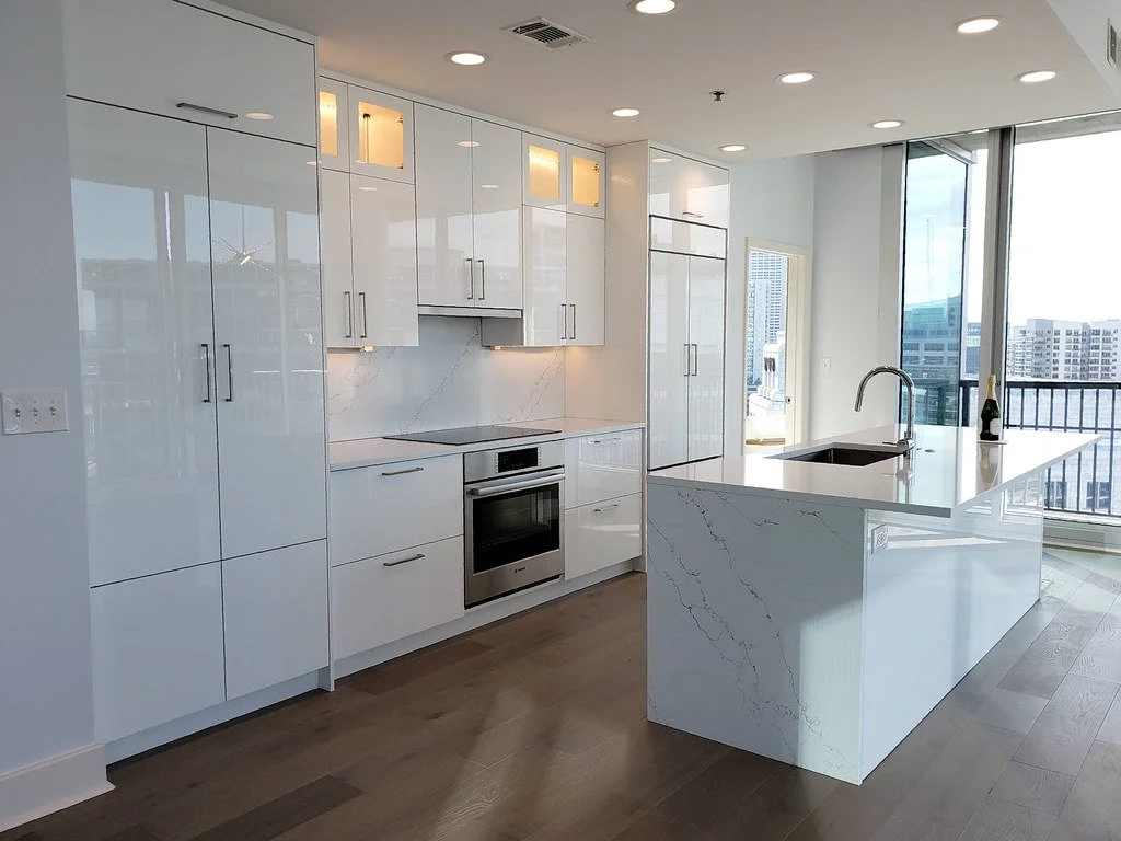 Modern kitchen with white high-gloss cabinets, marble countertops, stainless steel oven, island with a sink, large windows with city view.