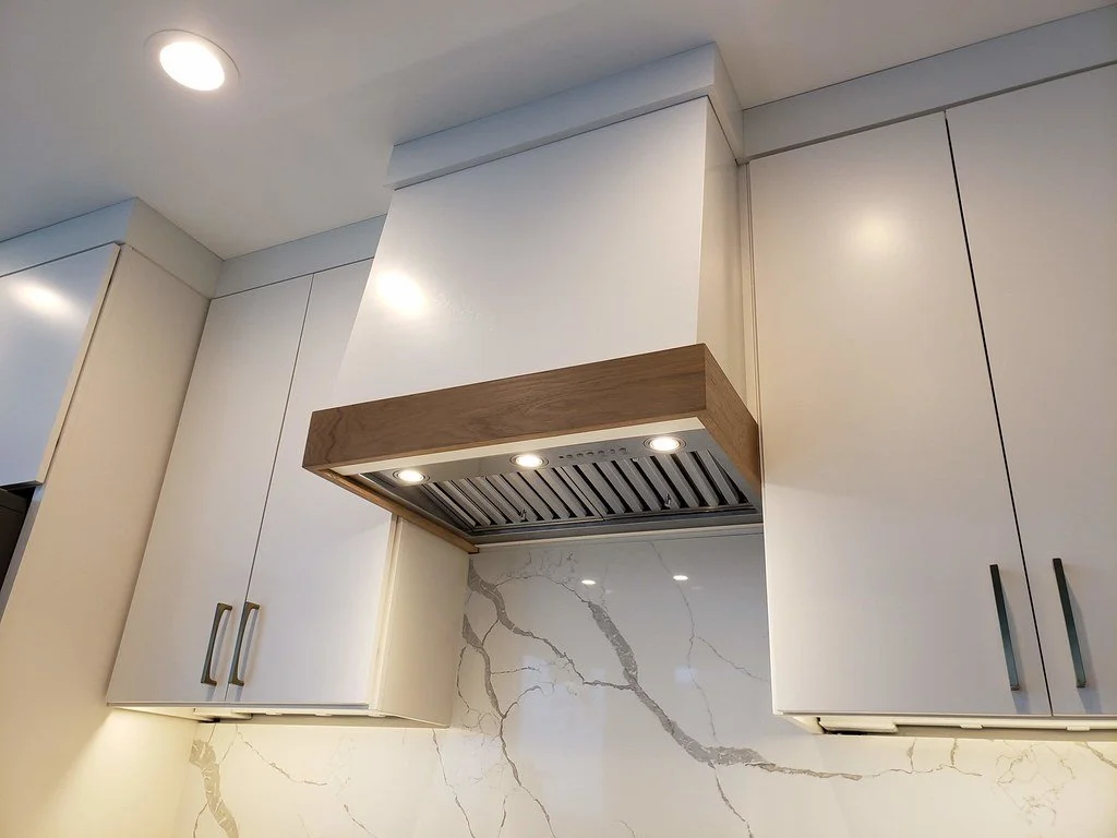 Kitchen ceiling with built-in white cabinets and a wooden range hood over a marble backsplash with gray veining.