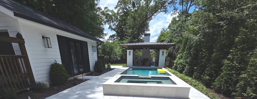 Backyard with small pool, hot tub, and an outdoor pavilion with seating, surrounded by trees.