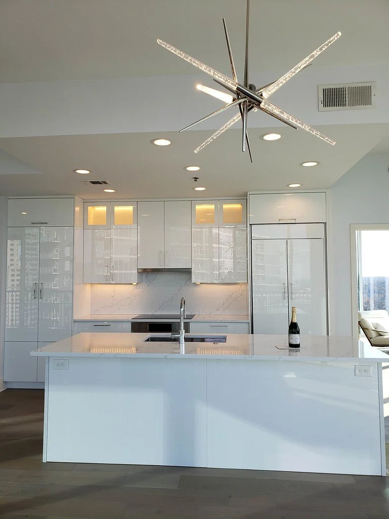 Modern kitchen with white cabinets and a marble backsplash, island with a sink, and a chandelier with multiple light bars hanging from the ceiling.
