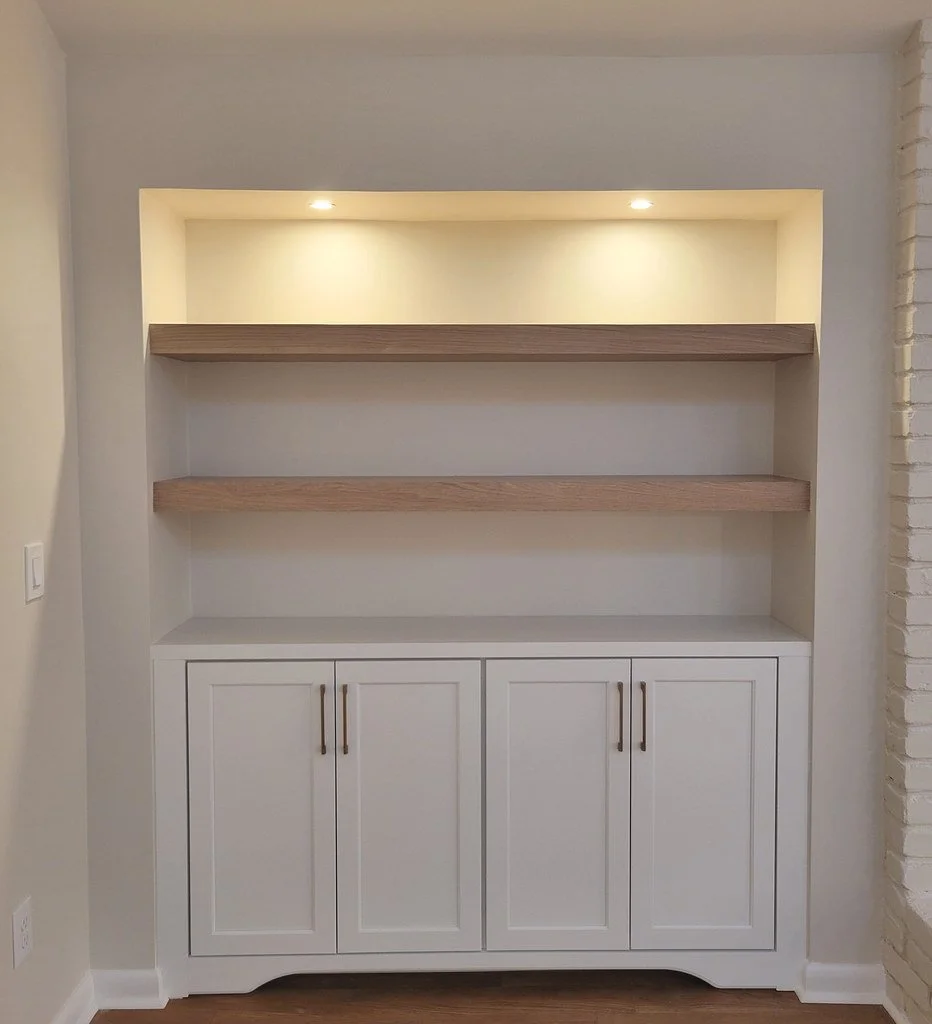 Built-in white cabinet with four doors at the bottom, three open shelves above, and recessed lighting at the top.