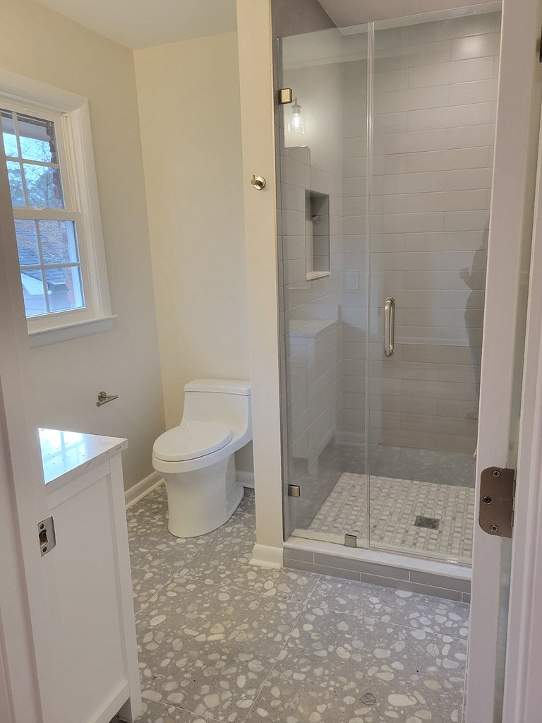Bathroom with a window, a modern toilet, and a glass-enclosed shower with light gray tiles and a built-in niche.