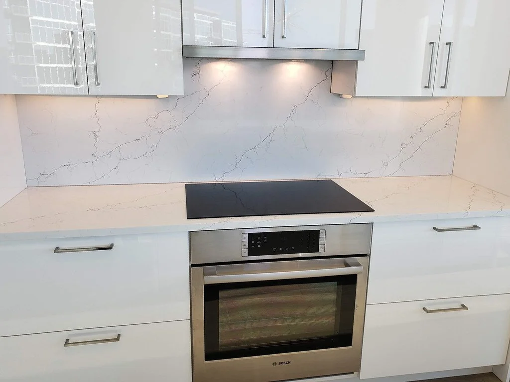 Modern kitchen with white cabinets, marble backsplash, and a built-in Bosch oven and cooktop.