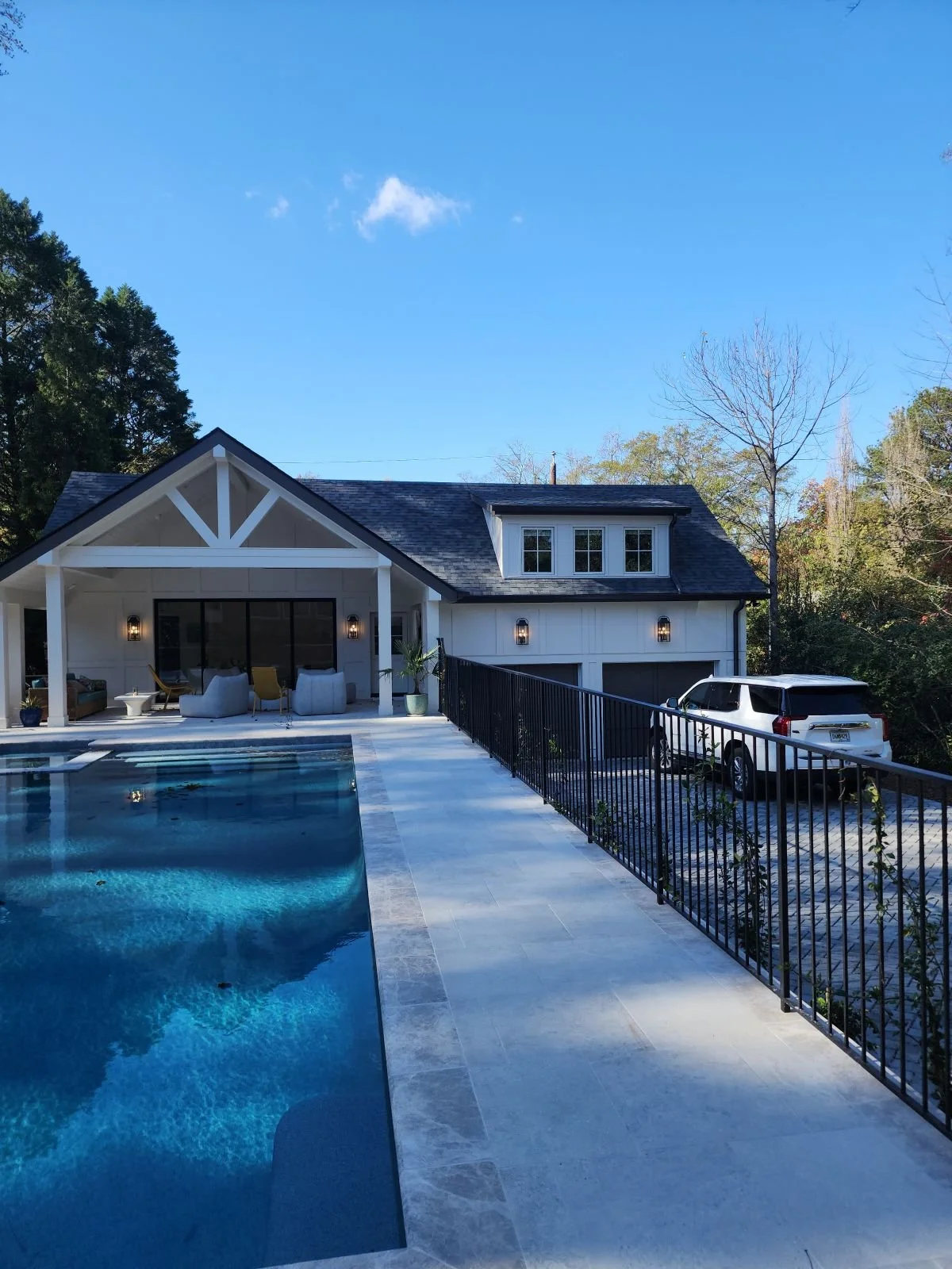 A modern house with a swimming pool in the backyard, a car parked in the driveway, and a clear blue sky.