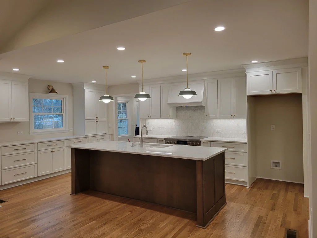 Modern kitchen with white cabinets, a large island with a dark wood base, pendant lighting, and hardwood floors.