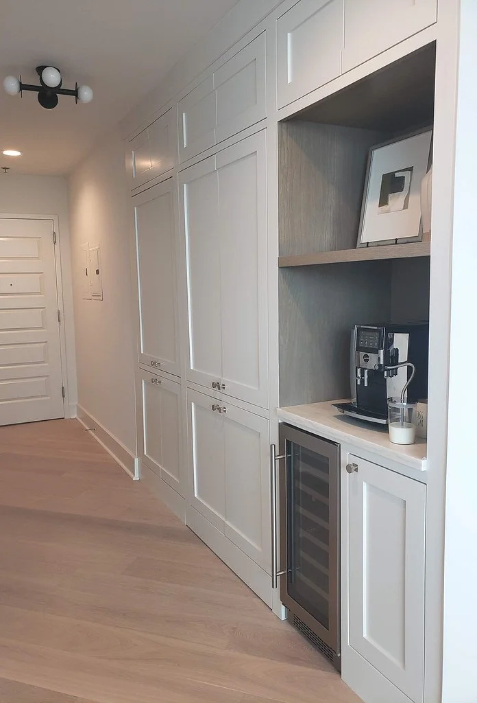 Kitchen area with white cabinetry, a built-in coffee machine, a small wine refrigerator, and shelves with artwork and decor.