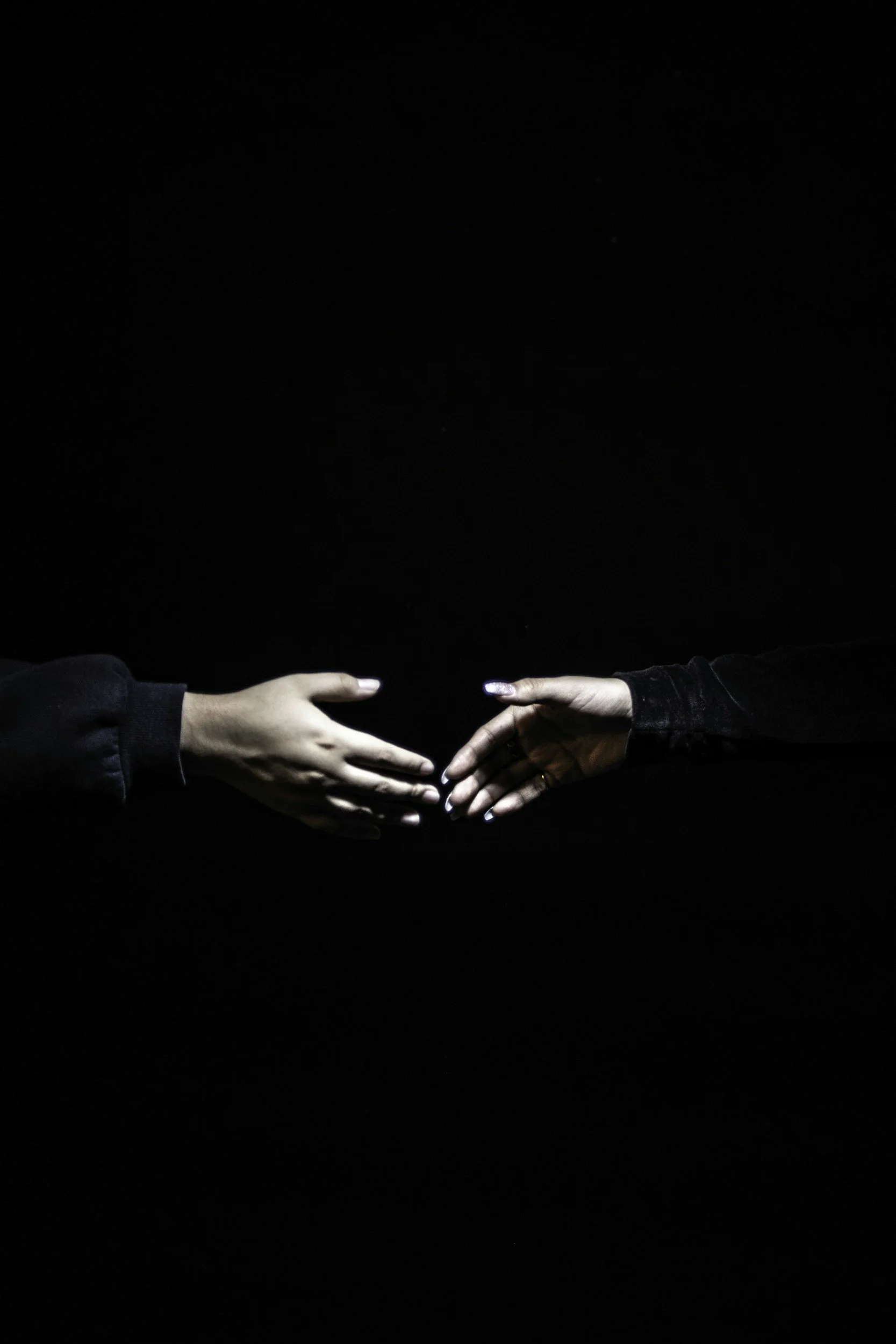 Two hands reaching out and nearly touching against a black background.