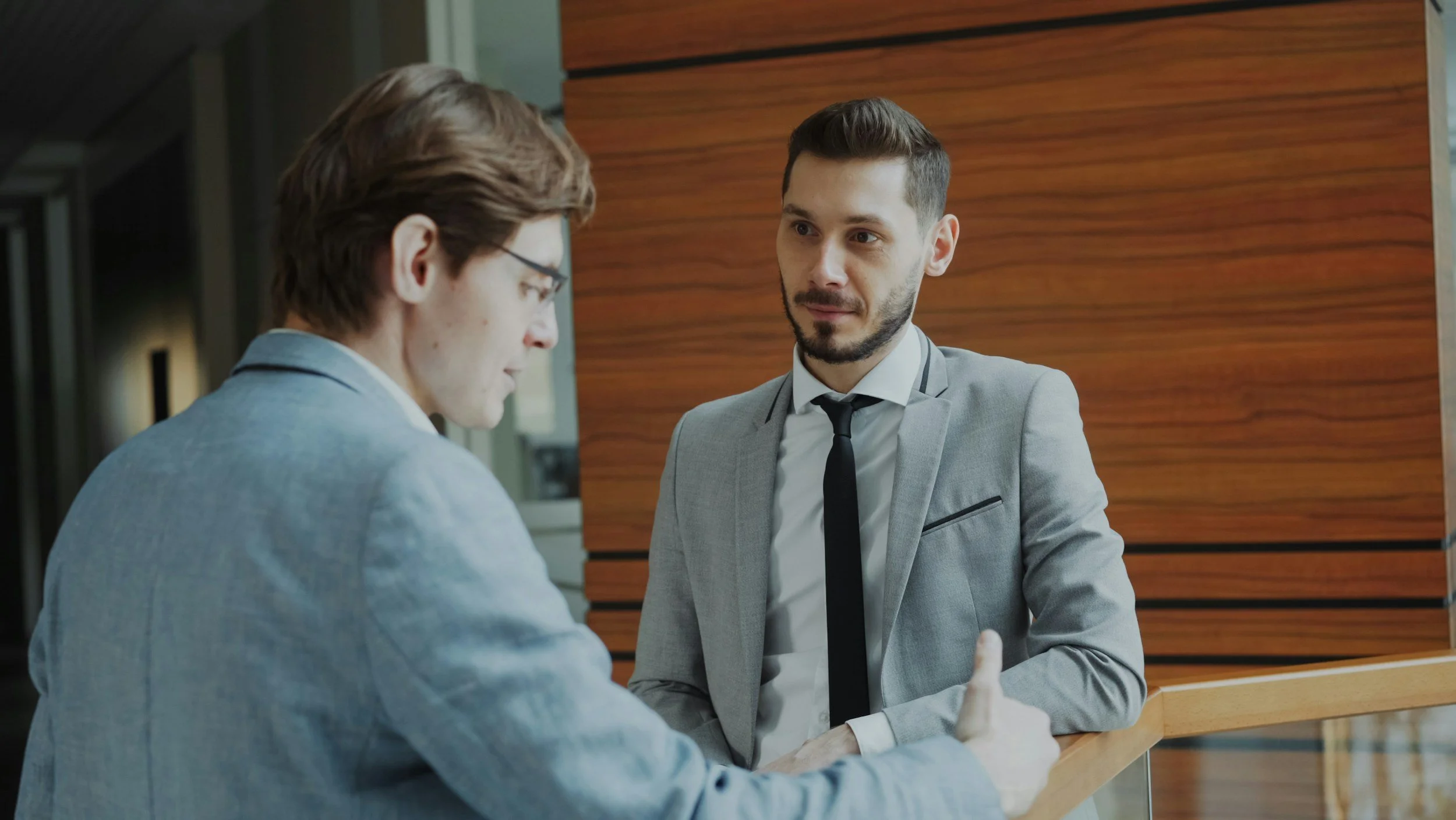 Two men in business suits having a conversation at a reception desk in a modern office building.