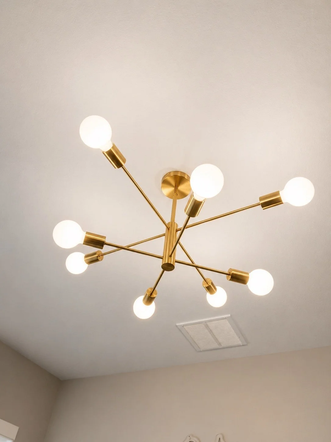 Modern chandelier with multiple exposed round light bulbs and gold fixtures hanging from a beige ceiling.