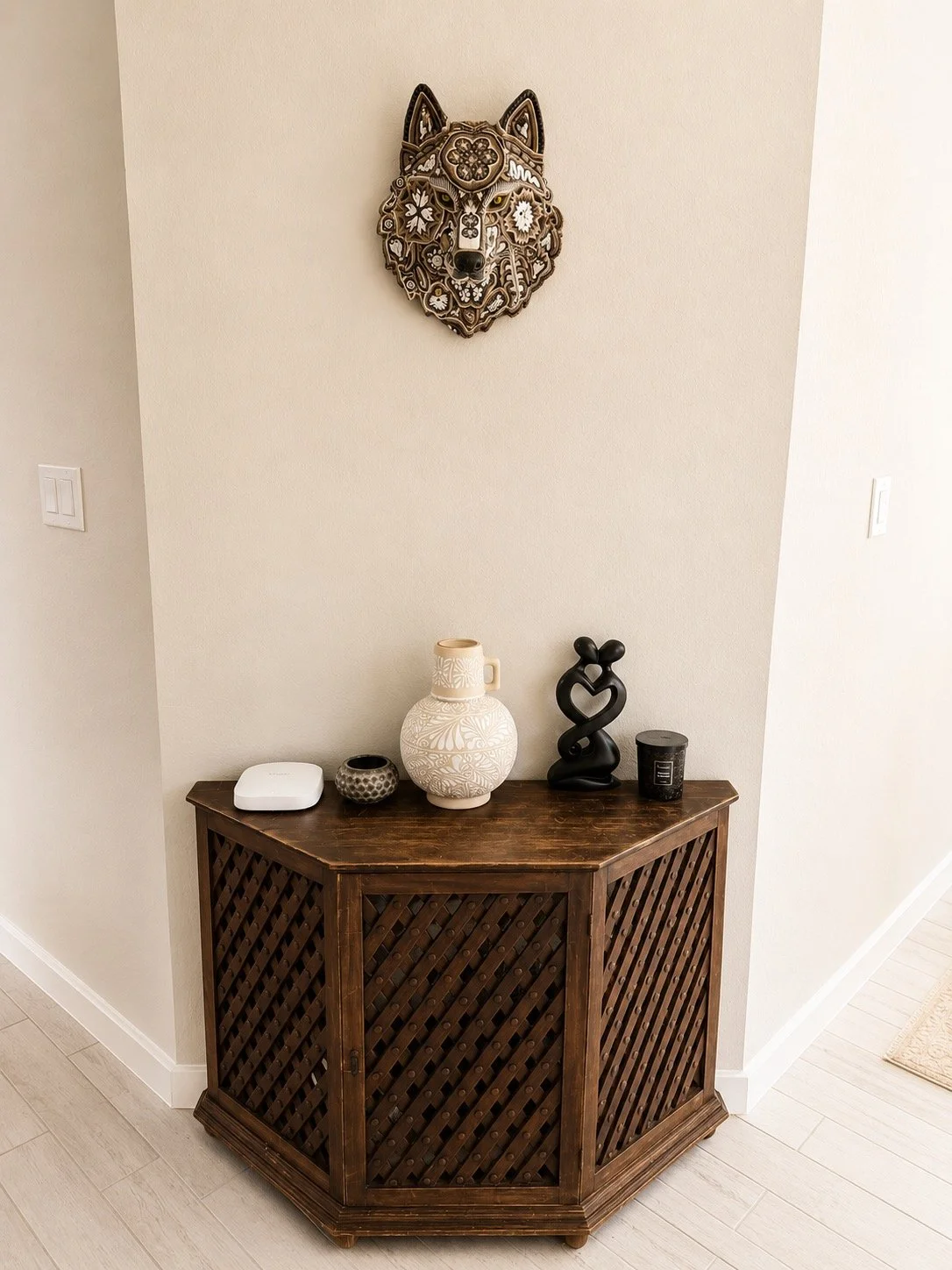 Decorative items on a wooden corner cabinet in a beige room with a wolf head wall art.