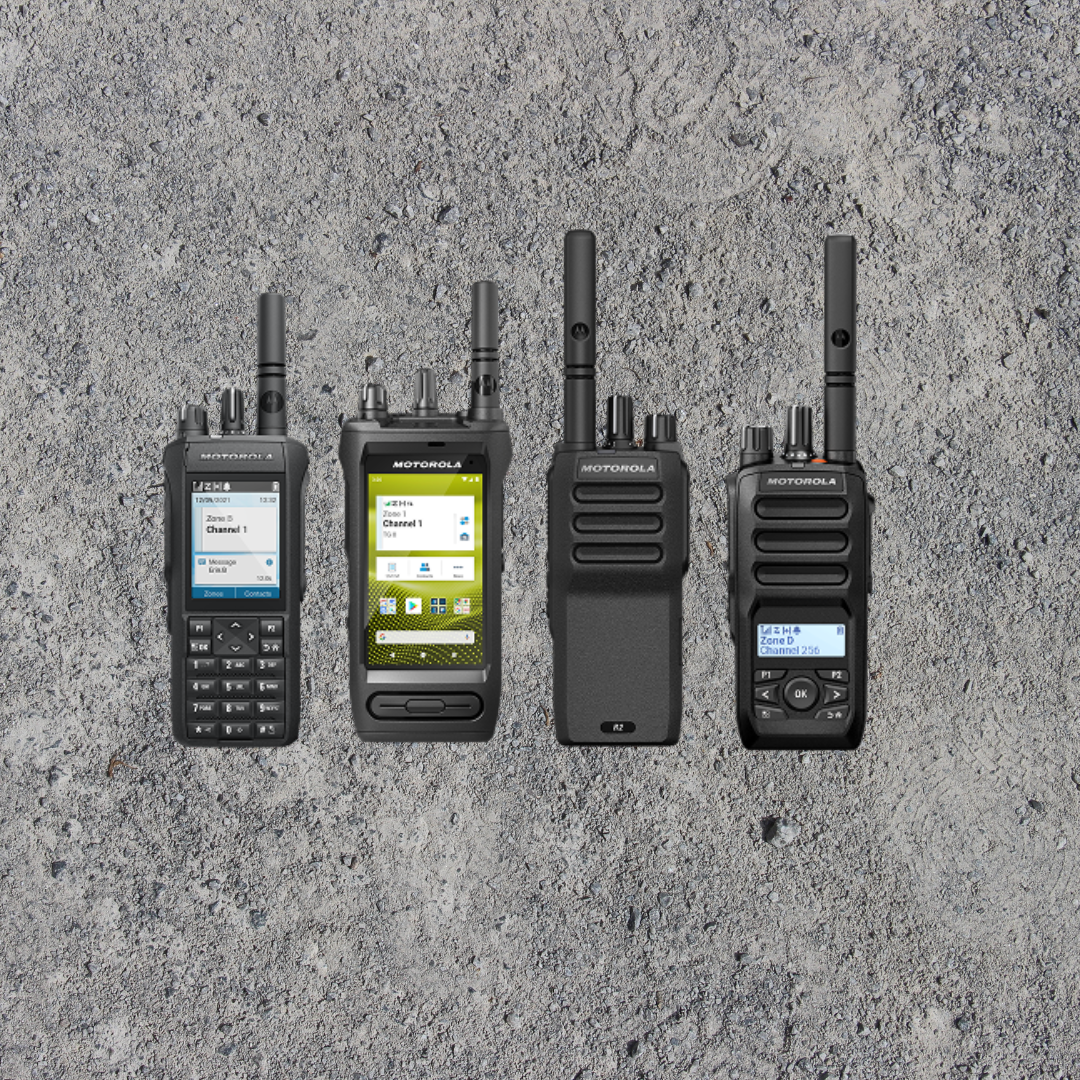 Four Motorola two-way radios with antennas placed on a textured gray surface.