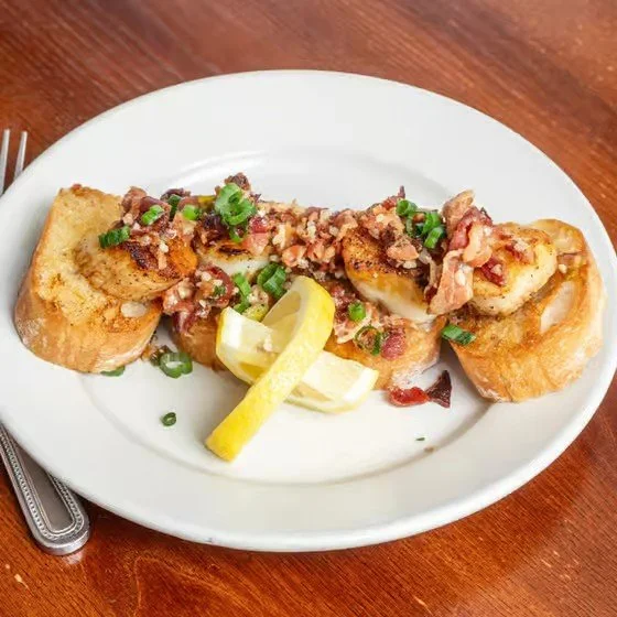 Fried fish fillets topped with bacon bits, green onions, and served with lemon wedges on a white plate