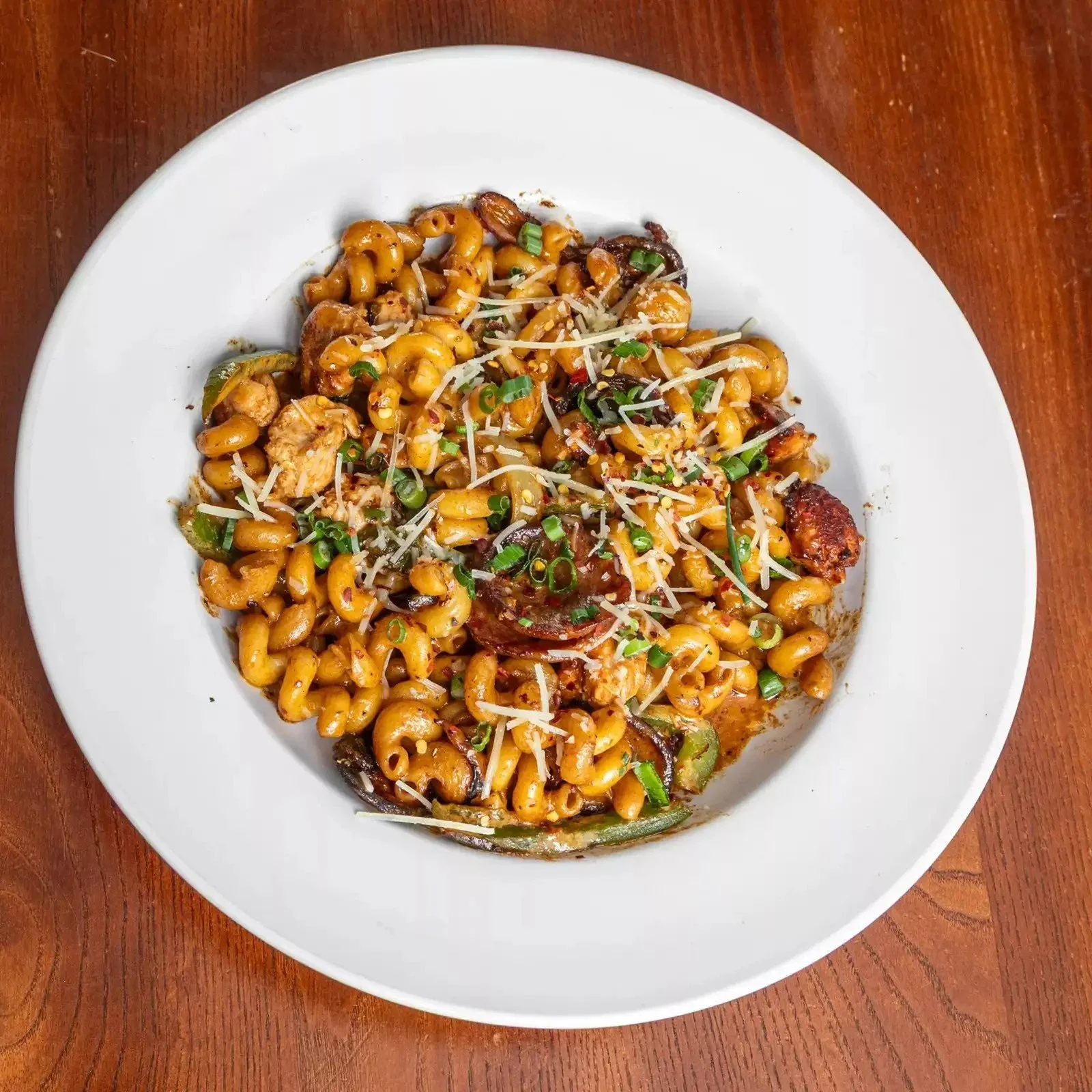 A white plate of mac and cheese with green onions and shredded cheese topping, on a wooden table.