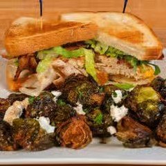 A club sandwich with turkey, lettuce, and tomato, served with roasted Brussels sprouts.