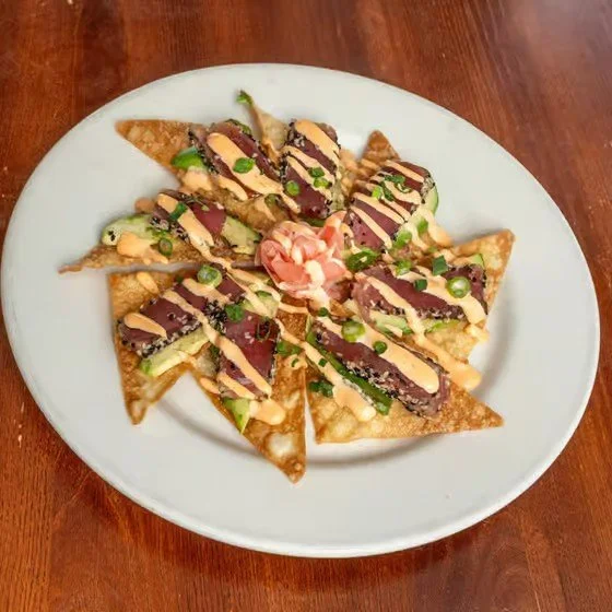 Plate of sliced crispy wontons topped with eel sauce, sliced green onions, and spicy mayo, garnished with a small amount of pickled ginger in the center