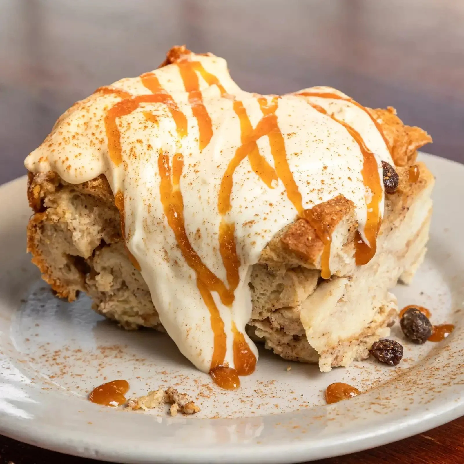 Close-up of a dessert with vanilla ice cream, caramel sauce, and crumbly cookie pieces on top and at the base, served on a white plate.