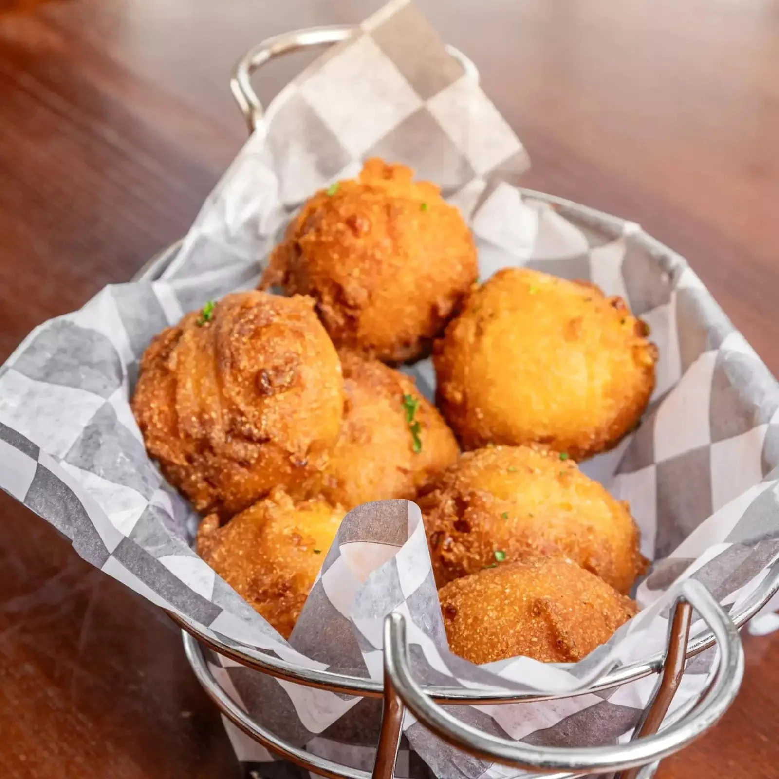 Fried cauliflower bites in a small metal basket lined with checkered paper on a wooden table.