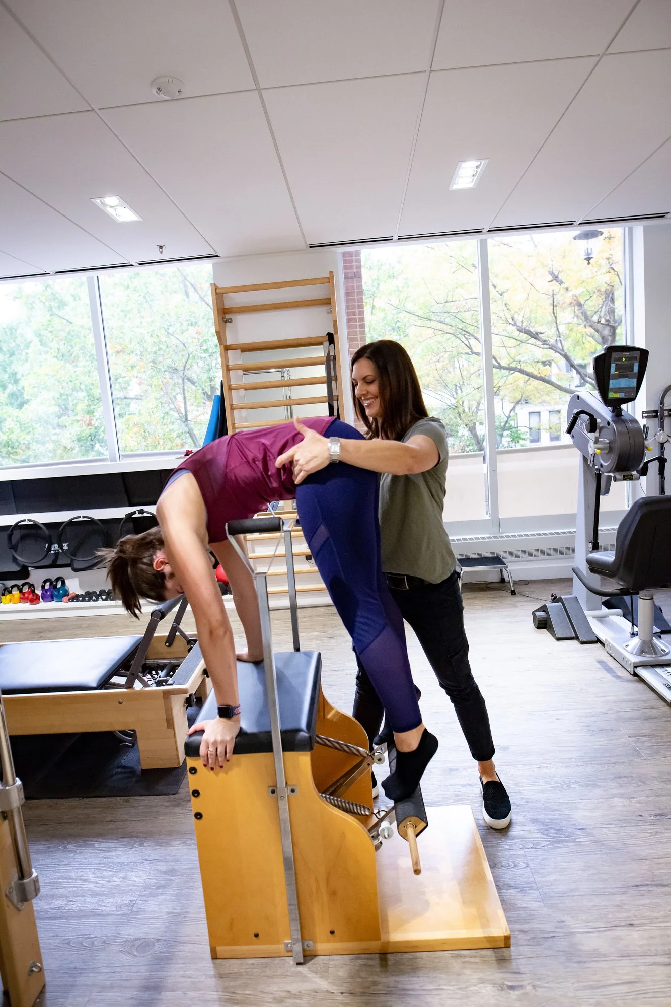 A physical therapist working with a patient on a reformer, with the patient doing clinical Pilates and the PT giving cues during movement