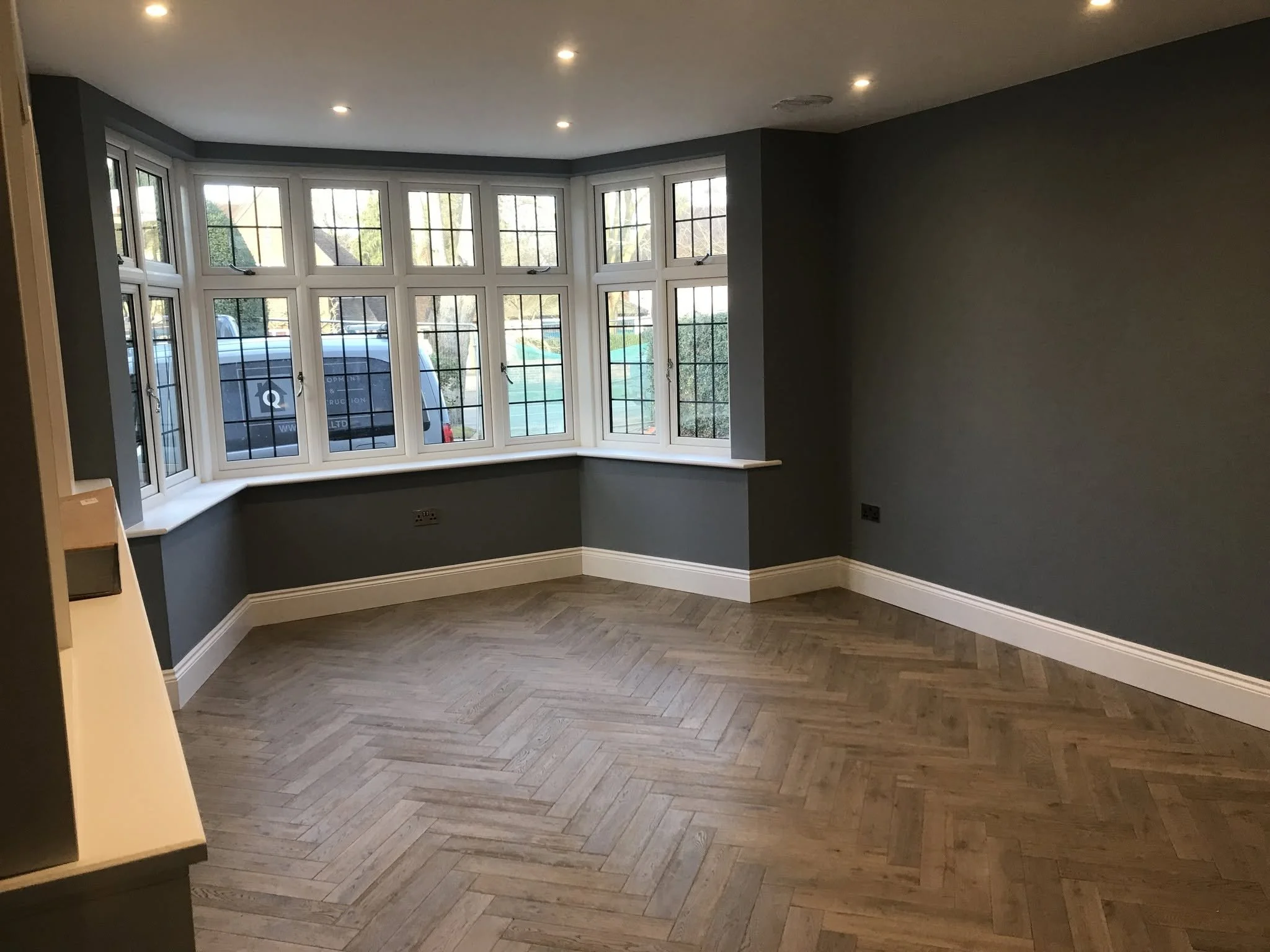 Interior of a room with gray walls, a large bay window with new wooden flooring and skirting boards