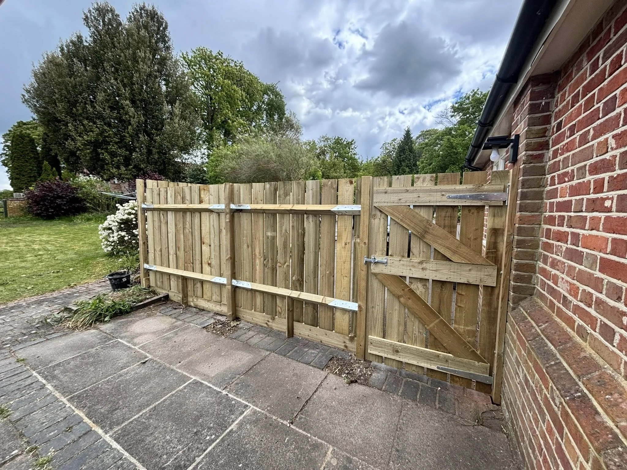 A wooden fence next to a brick house with a black gutter, overlooking a garden.