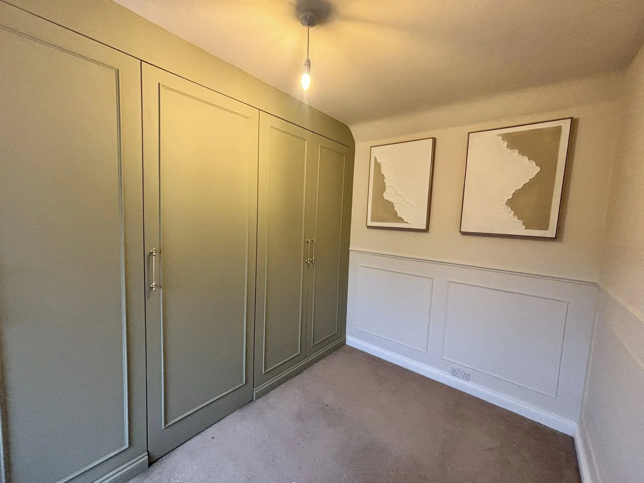 Built in green wardrobe next to a white wall with wood panelling.