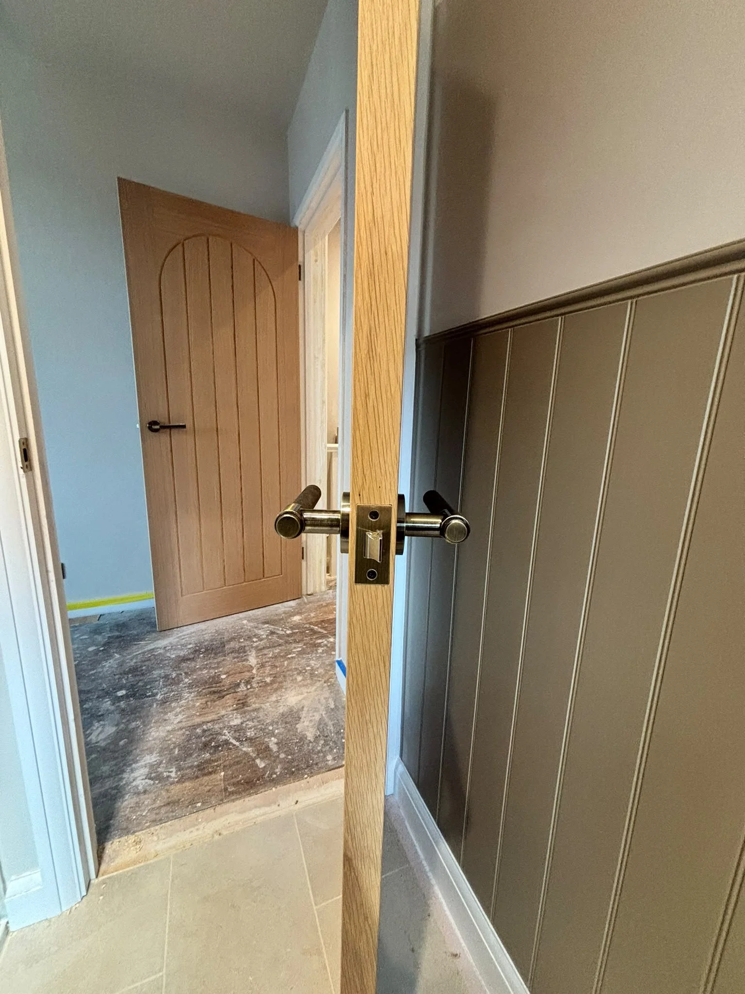 Interior view of a doorway with a wooden door, and grey wood panelling.