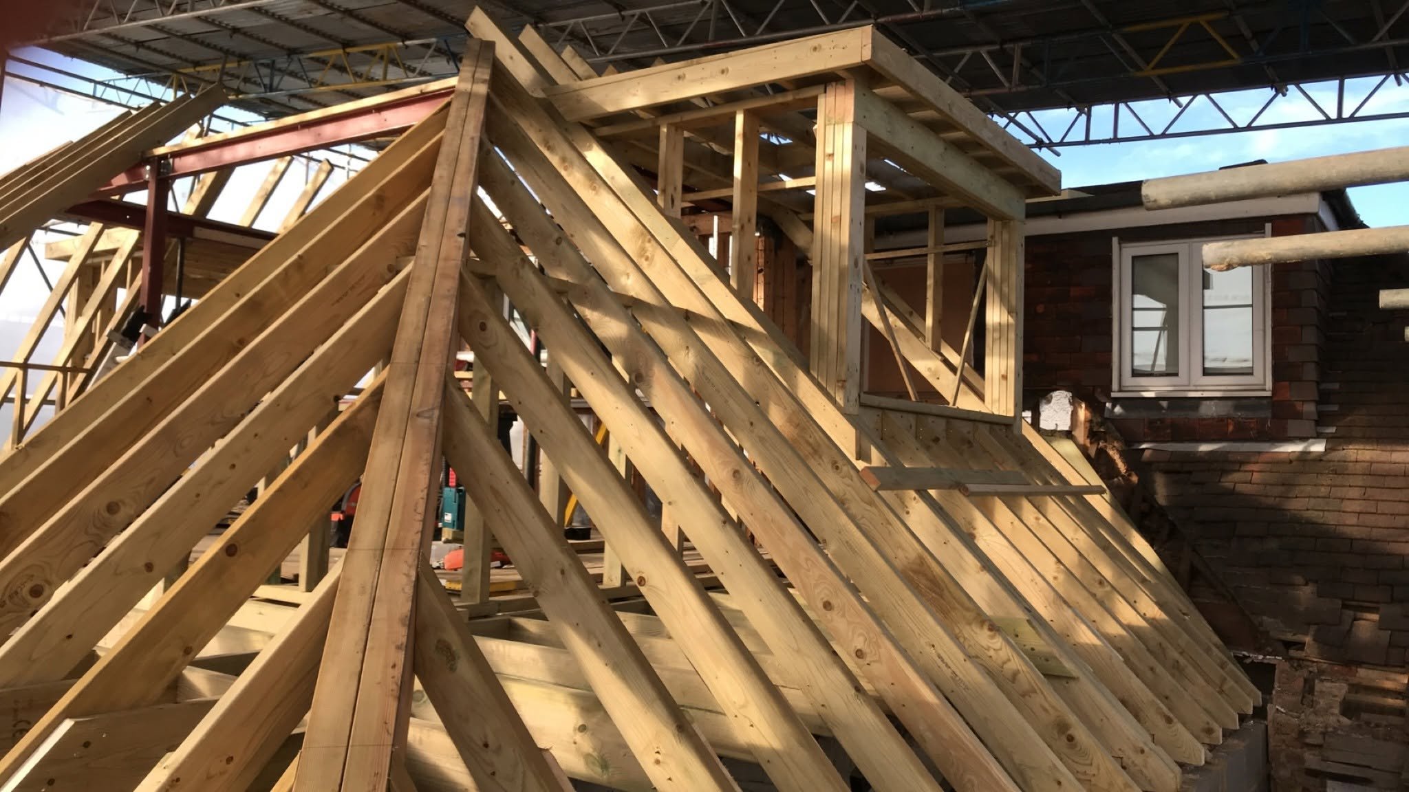 A view of a wooden roof being built with the dormer window the focus of the image.