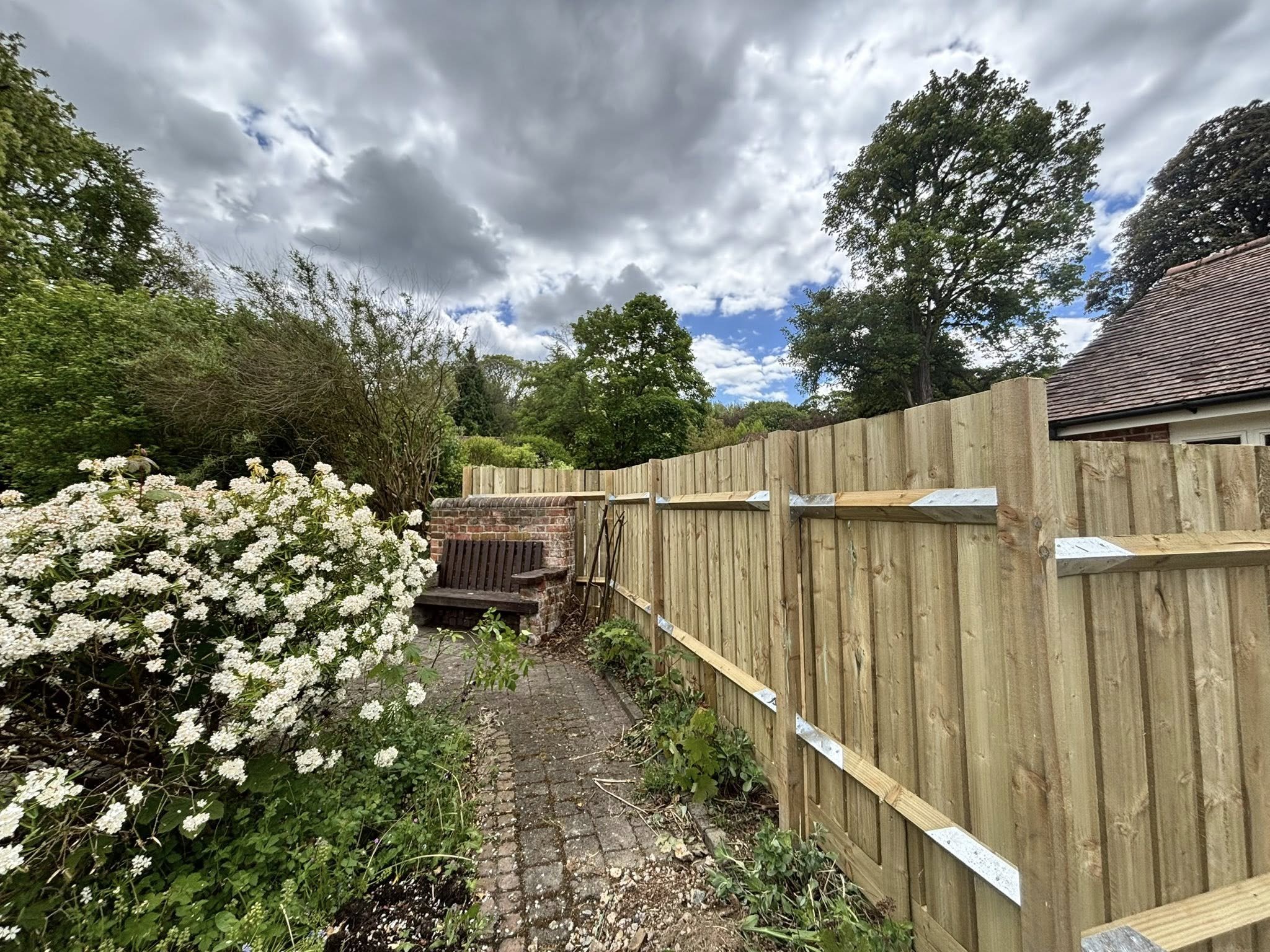A back garden with a new wooden fence that is going around a corner.
