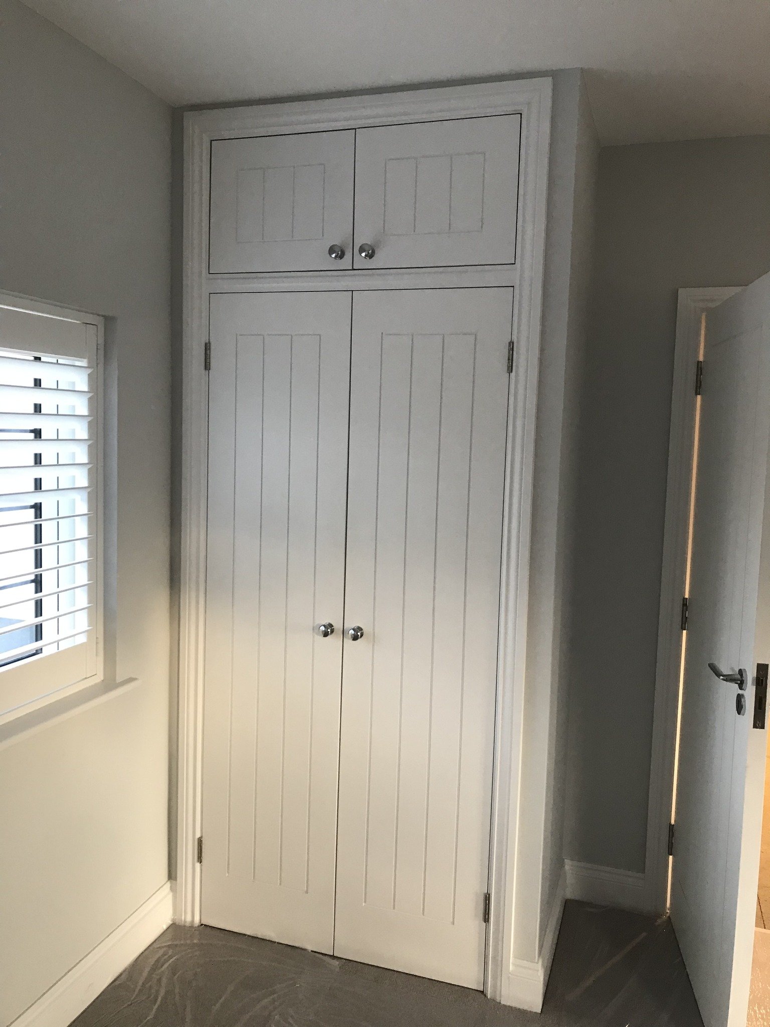 Built in white wardrobe in the corner of the room next to a window