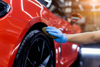 Person wearing blue gloves polishing a red car in a garage.