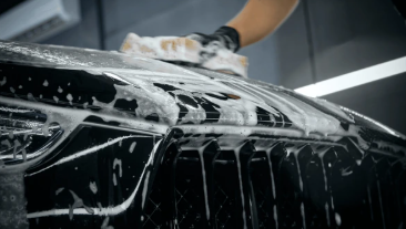 A person washing a black car with soap and a sponge in a car wash or detailing station.