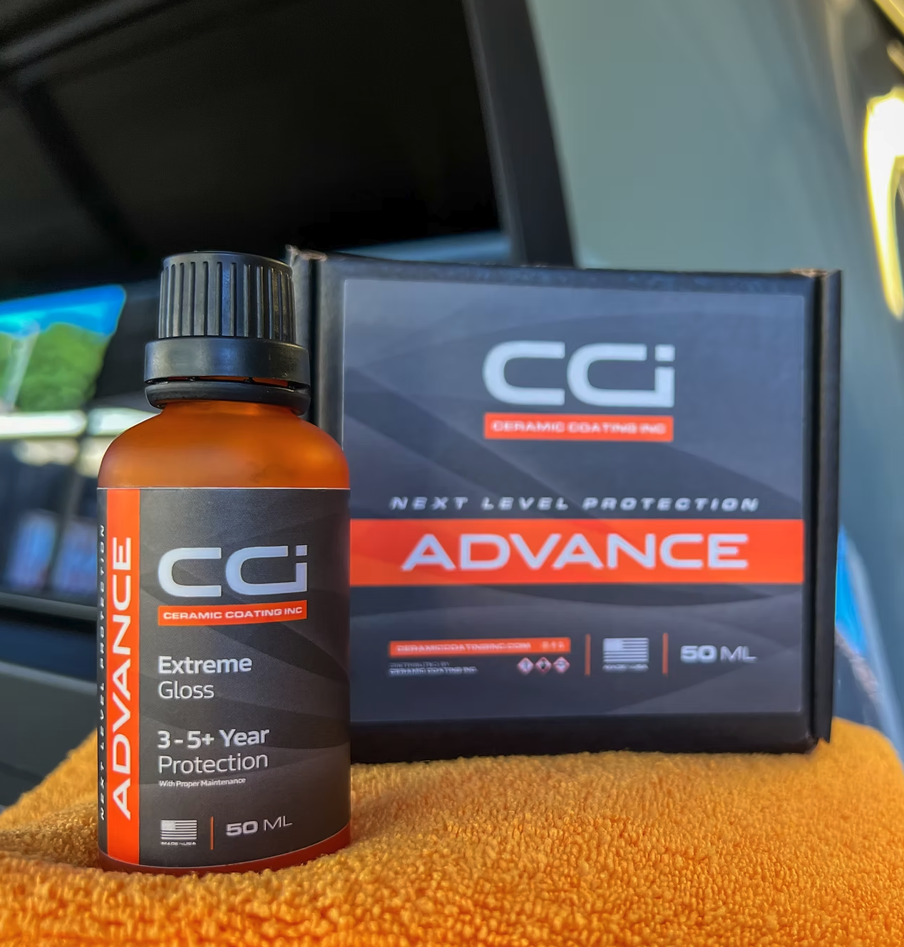 A bottle of CC Advance ceramic coating product labeled 'Extreme Gloss' with 50ML capacity, placed in front of a box of CC Advance ceramic coating, also labeled 'Extreme Gloss,' on an orange cloth.