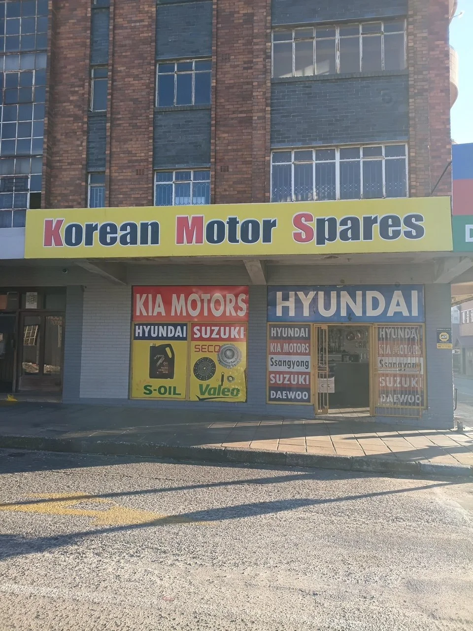 Storefront for Korean motor spares with signs for Kia Motors, Hyundai, Suzuki, SsangYong, Daewoo, and various car parts and oils.