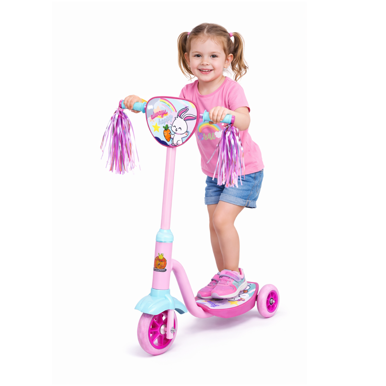 Niña feliz con vestido rosa y pantalones cortos montada en patineta rosa con ruedas rosas y decoraciones rosas y moradas, sosteniendo la empuñadura del patinete decorada con cintas de colores y dibujo de conejo.