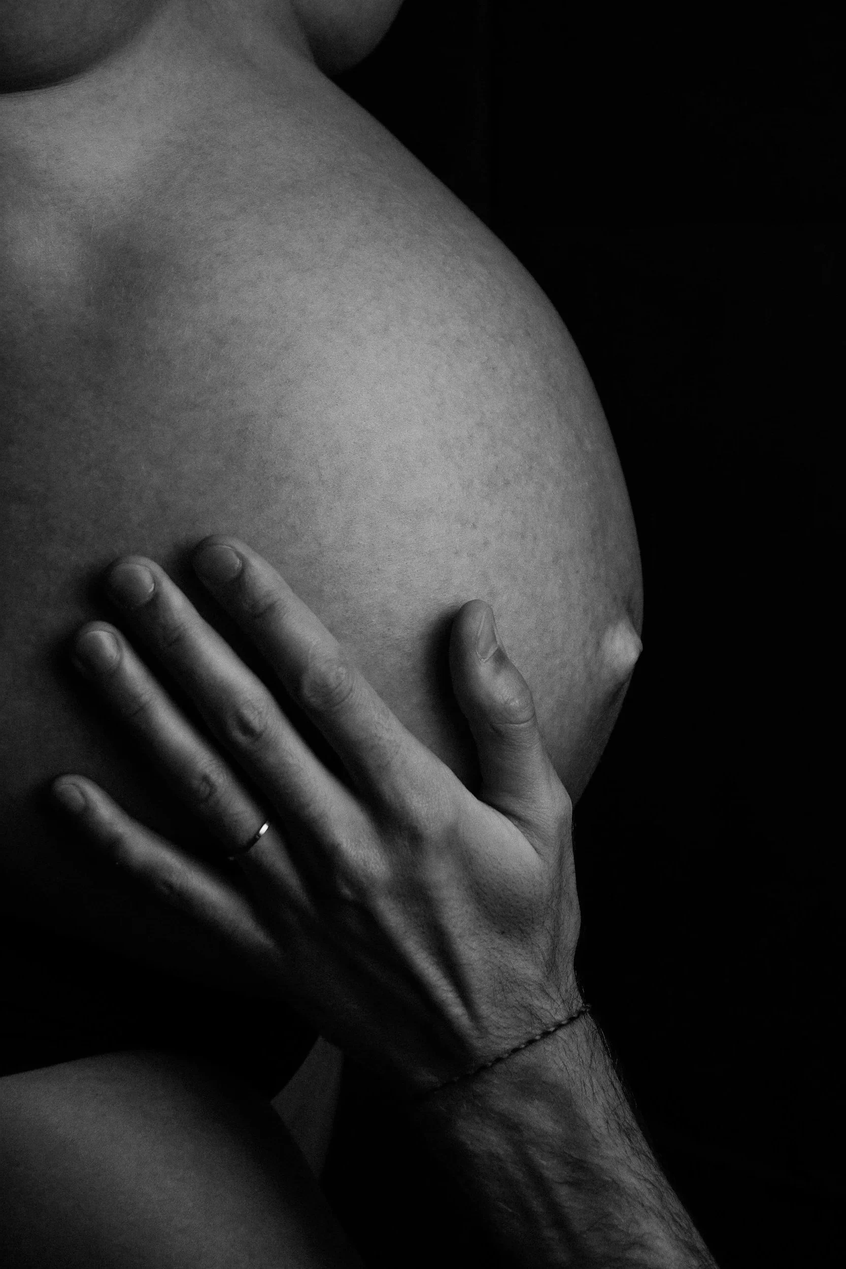 A close-up black and white photograph of a person's chest with a hand resting on it. The person's face is partially visible, but not detailed. The focus is on the chest and hand, with a dark background.