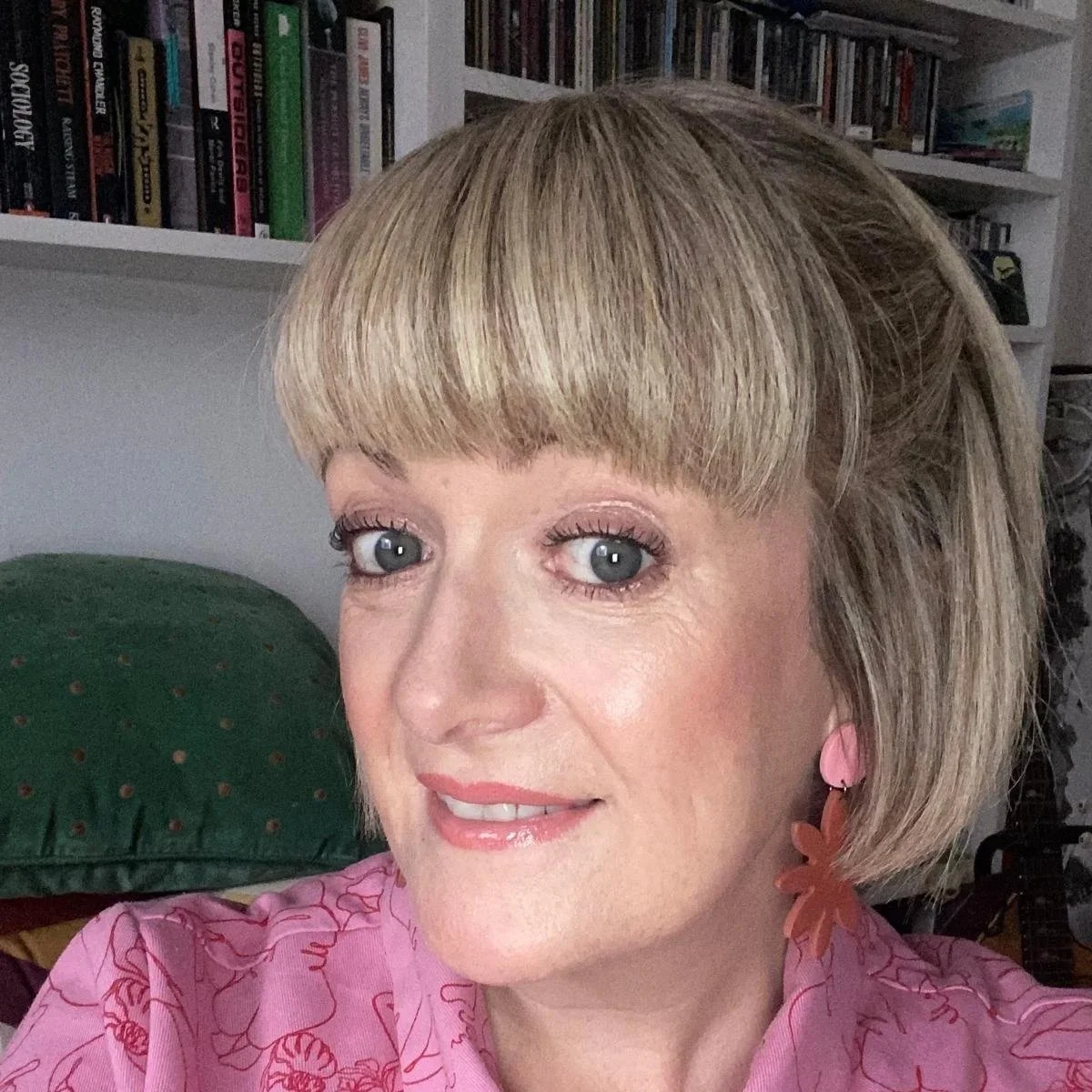 Sound Waves Choir member Vicky wearing a pink patterned top, smiling with a bookshelf in the background.